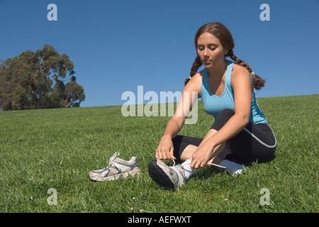 Jeune femme mise sur des chaussures d'athlétisme dans le champ Banque D'Images