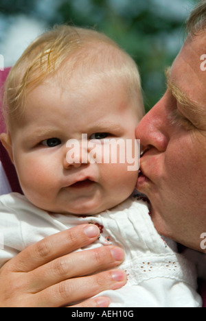 Close up portrait of vertical d'un bébé de six mois fille tirant une drôle de visage désapprobateur comme son père l'embrasse sur la joue Banque D'Images