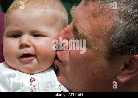 Close up portrait of horizontal de bébé de six mois fille tirant une drôle de visage désapprobateur comme son père l'embrasse sur la joue Banque D'Images