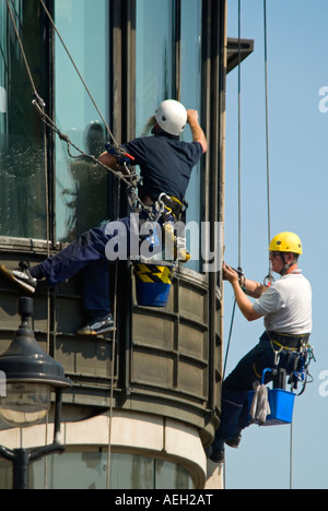 Close up vertical de deux windowcleaners se balançant dangereusement à nettoyer les vitres Banque D'Images