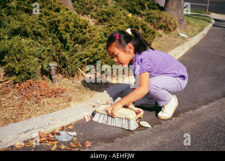 Fille 5-7 ans balayant le brossage allée fond feuilles corbeille corvée se baissant multi multiculturelle diversifiée ethniques de la diversité multiculturelle raciale Banque D'Images