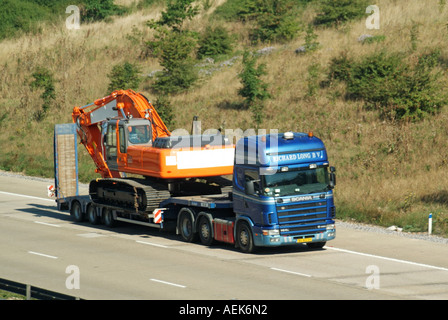 Camion Scania hgv et remorque basse chargeuse chargée avec pelle de pose de chenilles conduisant le long de la route d'autoroute en béton britannique dans Essex Angleterre Royaume-Uni Banque D'Images