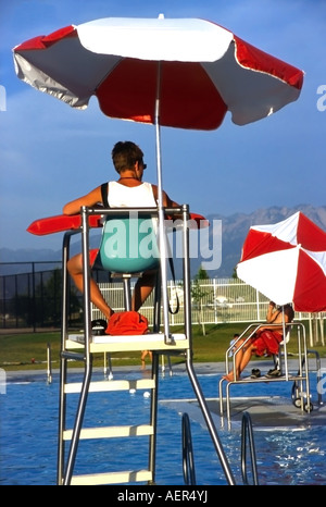 Ce maître-nageur est alerte, et ombragé sous son parapluie à une piscine publique de l'Utah, USA, mais près de l'heure de fermeture il a peu à faire. Banque D'Images