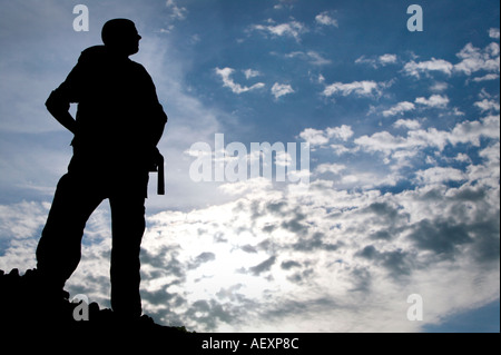 Portrait d'un homme adulte debout sur un tas de roches. Il est découpé sur un fond bleu, ciel nuageux. Plan horizontal. Banque D'Images