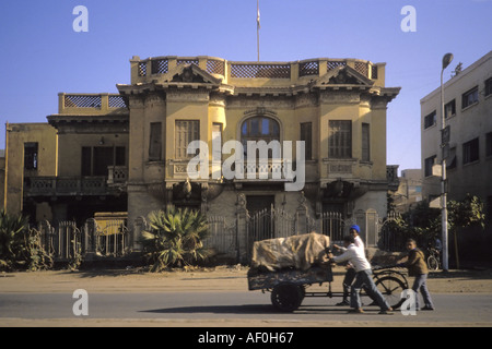 Trois garçons pousser un chariot vers le bas un Égyptien street en face d'un bâtiment colonial. Banque D'Images