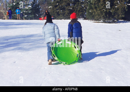 New York, Central Park, neige. Cedar Hill deux jeunes filles avec un traîneau grimpant sur une pente enneigée. Monter une colline en hiver dans la ville de New York aux États-Unis Banque D'Images