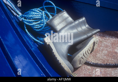 Close up de noir-gris bottes gisant dans proue de bateau peint bleu avec bobine de corde en nylon bleu clair Banque D'Images