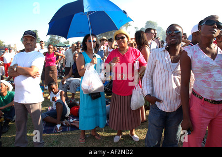 Groupe multiculturel à l'abri du soleil sous un parapluie à l'écoute de concert en plein air à Brockwell Park dans le sud de Londres. Banque D'Images