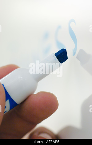 Close-up of hand holding marqueur bleu écrit sur un tableau blanc Banque D'Images