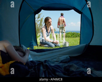 Vue à travers l'ouverture de la tente avec les jeunes femmes à l'intérieur de dormir pendant que l'autre à l'extérieur de cuisiniers avec un jeune homme debout Banque D'Images