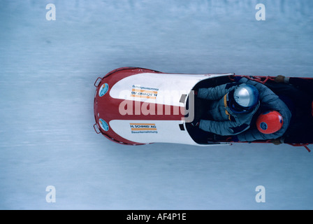 Deux hommes tobogganists dur banque autour d'une courbe verticale en vitesse sur la Cresta Run St Moritz l'Engadine Suisse Banque D'Images