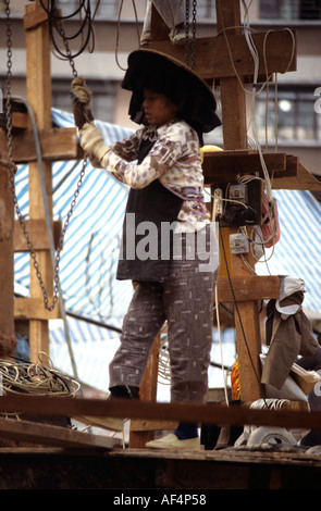 Une femme ronde large Hakka en chapeau noir avec frange pendaison travaillant sur chantier, à la fin des années 70, Hong Kong Banque D'Images