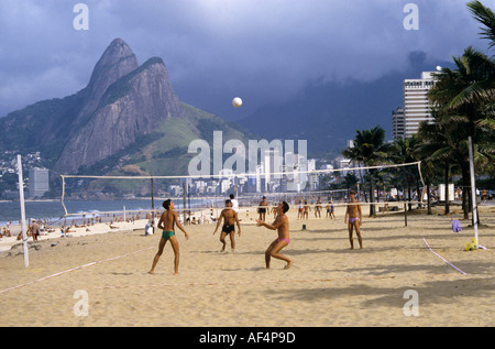 Quatre jeunes hommes jouer au volley-ball sur la plage d'Ipanema avec vue mer et collines de forme inhabituelle au-delà de Rio de Janeiro Brésil Banque D'Images