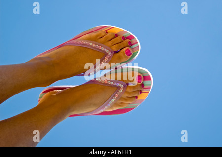 Close up horizontal de peau tannée pieds avec des ongles peints à rayures portant des tongs contre un ciel bleu Banque D'Images