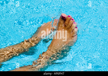 Close up horizontal de peau tannée les pieds mouillés avec des ongles peints aux éclaboussures autour d'une piscine bleu vif Banque D'Images