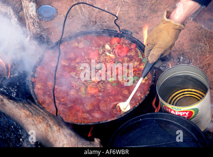 Un cowboy cuisinier prépare un ragoût de chili cowboy sur un feu de camp dans une cocotte sur un transport de bétail sur un grand ranch de bétail Banque D'Images