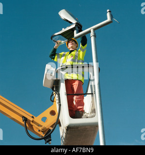 Homme debout sur grue de travail élevées et plate-forme, le maintien d'une lumière de rue. Banque D'Images