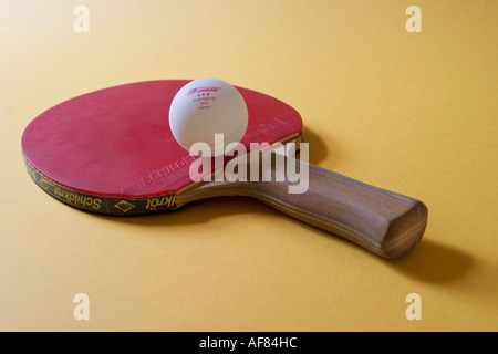 Raquette de tennis de table avec balle de ping-pong qui s'y repose sur un fond jaune Banque D'Images