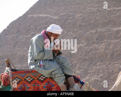 L'homme égyptien assis sur un chameau en face d'une pyramide de Gizeh, d'allumer une cigarette, l'Égypte, Le Caire, Gizeh, Gizeh, Giseh Banque D'Images