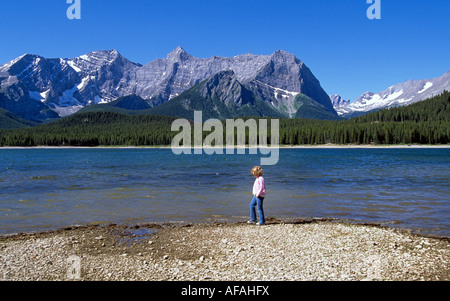 Une jeune fille se tient sur le rivage d'un lac de montagne dans la région de Kananaskis des Rocheuses canadiennes, l'Alberta, Canada. Banque D'Images