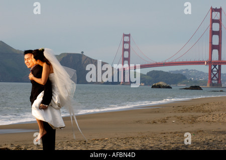 Marié mariée donnant Piggy Back Ride sur Baker Beach à San Francisco Californie le Golden Gate Bridge Banque D'Images