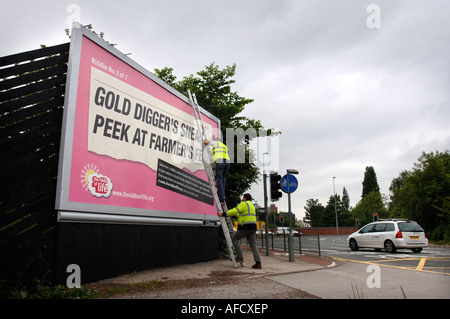 Deux travailleurs COLLER EN PLACE UN PANNEAU D'AFFICHE AVEC UN MESSAGE CRYPTIQUE DE LA BIBLE RELIGOUS À MANCHESTER UK Banque D'Images