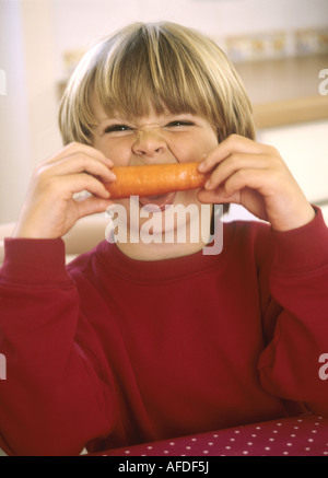 Jeune garçon assis dans une cuisine avec une carotte - s'amusant Banque D'Images