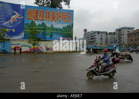 L'homme de la trottinette avec des panneaux dans l'arrière-plan, la ville de Guilin, Guangxi, Chine. Banque D'Images