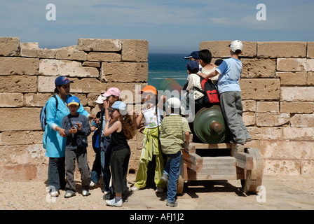 Collégiens le voyage d'une journée à jouer sur un canon vieux remparts Skala de la Ville Essaouira Maroc côte atlantique de l'Afrique du Nord Banque D'Images