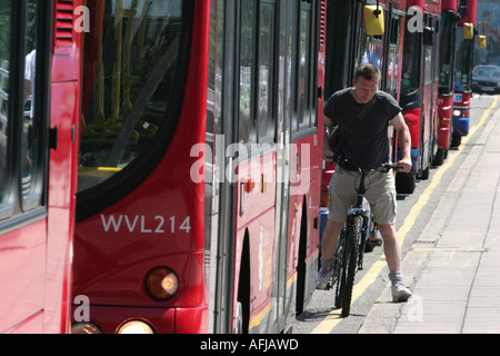 Un cycliste tisse entre les bus à Londres UK Banque D'Images