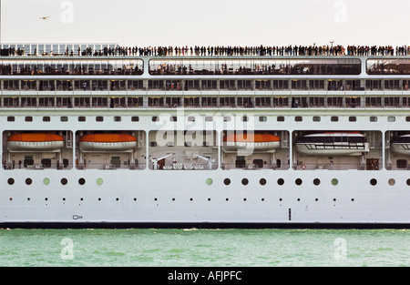 Côté d'un grand bateau de croisière avec beaucoup de gens visibles le long du pont de radeaux sur le côté et un petit avion volant au-dessus Banque D'Images