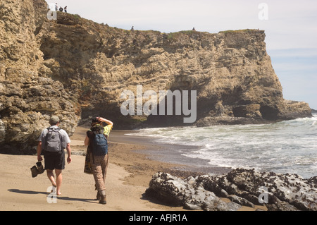 Homme et une femme avec des bottes de randonnée à pied vers Arch Rock avec des gens en haut le long de la plage Kellum Point Reyes National Seashore Banque D'Images