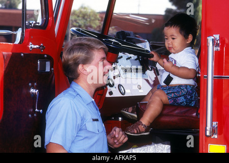 Fireman assiste à peu garçon Oriental au volant d'incendie moteur. Redondo Beach, CA. USA Banque D'Images