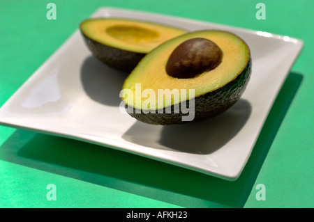 Graphique de style carte postale d'un coup de tranches d'avocat sur plaque carrée blanc, fond vert. Banque D'Images