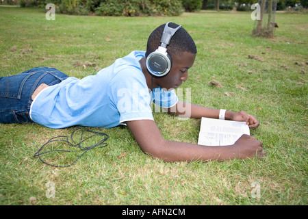 Jeune homme noir couché dans l'herbe à écouter de la musique et la lecture d'un livre Banque D'Images