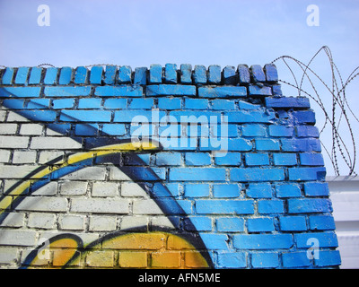 Coin de colorés couverts de graffitis mur de briques avec du fil de fer barbelé et ciel bleu Banque D'Images