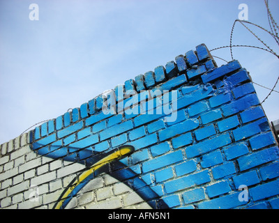 Coin de colorés couverts de graffitis mur de briques avec du fil de fer barbelé et ciel bleu Banque D'Images