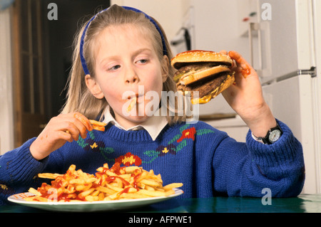 Junk food jeune écolière adolescent mangeant un énorme hamburger et chips buvant du coke à la maison dans après l'école Londres HOMER SYKES Banque D'Images