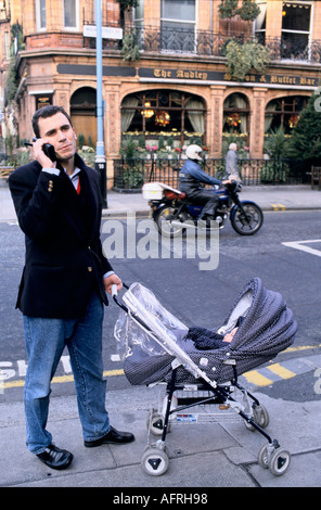 1980s Man UK. Père poussant bébé buggy enfant dans la poussette. Faire un appel téléphonique sur son téléphone portable rétro circa 1985 Mayfair Londres Angleterre HOMER SYKES Banque D'Images