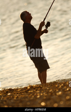 Une silhouette d'un homme de la pêche à la ligne de pêche sur la plage, dans la lumière du soir en été à Cowes sur l'une des plages de l'île de Wight Banque D'Images