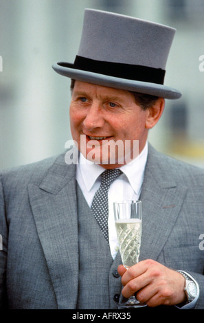 Homme des années 1980 en costume gris loué chapeau et manteau de parole, tenant un verre de champagne au Derby Epsom Downs 1985 Angleterre HOMER SYKES. Banque D'Images