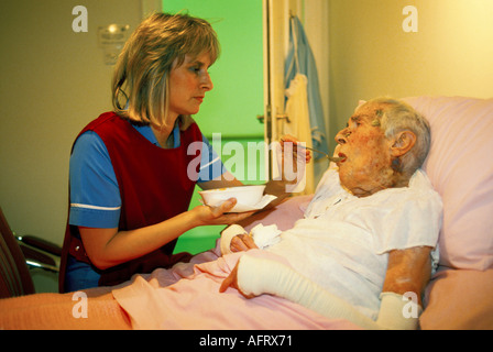 Care Home UK, le personnel infirmier nourrit une résidente âgée qui est couchée au lit. Années 1990 Cirencester Gloucestershire 1991 HOMER SYKES Banque D'Images