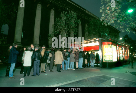 Paris France adultes français en ligne à l'extérieur de votre achat de billet de théâtre : Kiosque de la Place de la Madeleine éclairés la nuit, File d'attente Banque D'Images