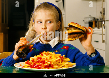 Adolescente jeune écolière mangeant un énorme hamburger et chips malbouffe, elle boit du coke à la maison dans après l'école Londres HOMER SYKES Banque D'Images