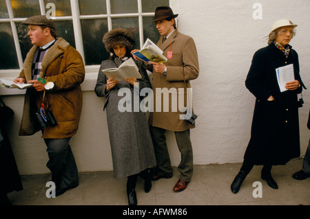 Grand National Aintree 1980s UK, les coureurs étudient leurs cartes de course. Habillé à la mode pour la journée aux courses. ANNÉES 80 ROYAUME-UNI HOMER SYKES Banque D'Images