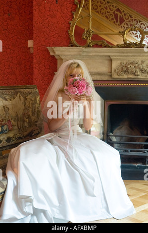 Mariée en satin brodé robe de mariage avec Tiara et simple voile assis sur un canapé recouvert de tapisserie dans la salle élégante Banque D'Images