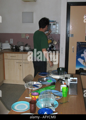 Jeune homme de race blanche à l'aide de micro-ondes dans un appartement étudiant. Banque D'Images