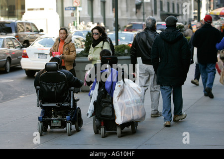 Les personnes handicapées en fauteuil roulant motorisé de shopping en voiture le long du trottoir au travers des foules de personnes Banque D'Images