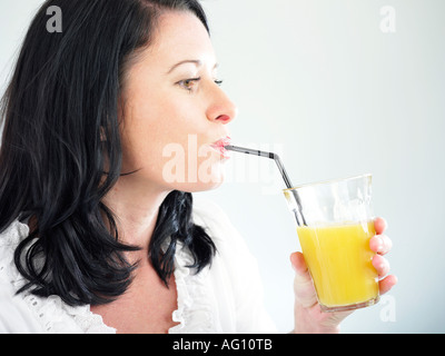 Femme buvant un grand verre de jus d'orange frais grâce à la paille Banque D'Images