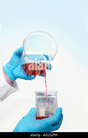 Red Scientist pouring liquid into beaker, close-up of hands Banque D'Images